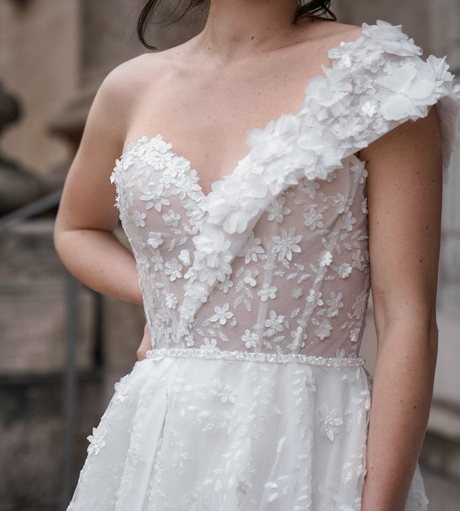 Détail du corsage à fleurs brodées et de l’épaule unique de la robe de mariée EUGENIA, collection Éclat Royal, atelier AM LUX COUTURE à Lyon